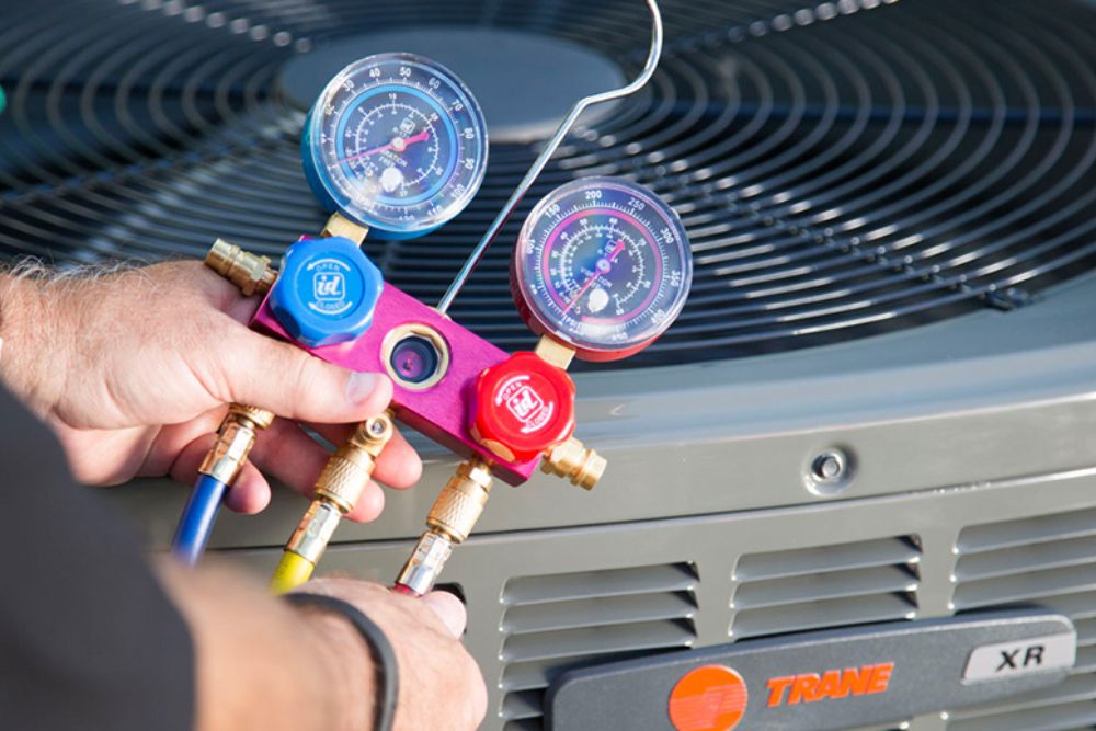 A technician in Los Angeles, CA, holds a hose and gauges while working on an HVAC unit for heating and air conditioning.