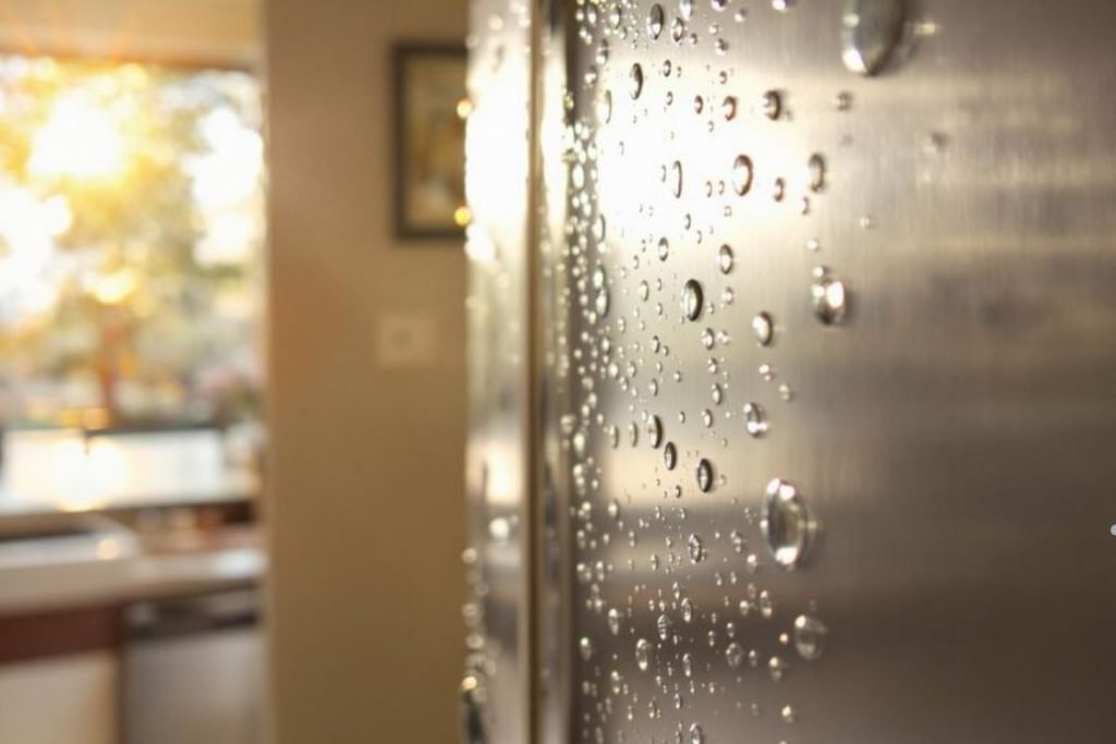 A refrigerator door glistening with water droplets, reflecting light and showcasing a cool, refreshing appearance.