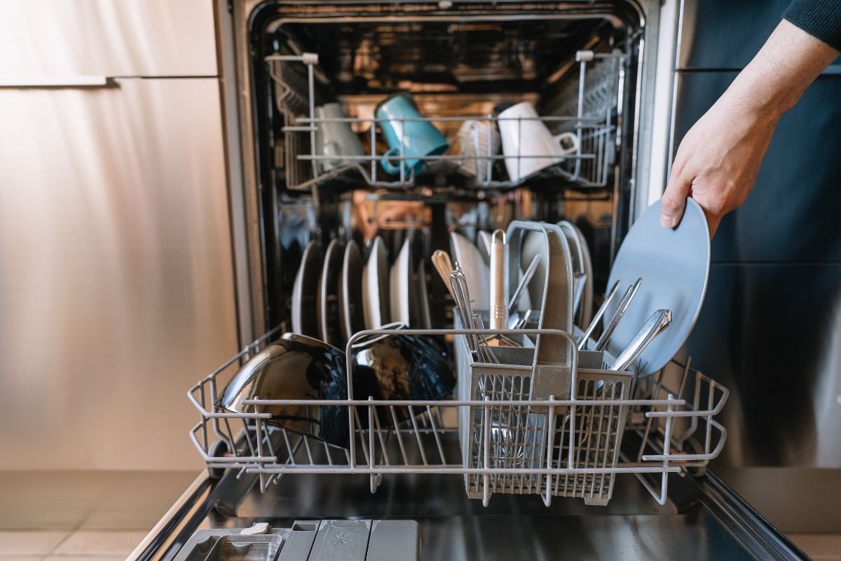 An individual is holding a dish while standing next to an open dishwasher, ready to load it.