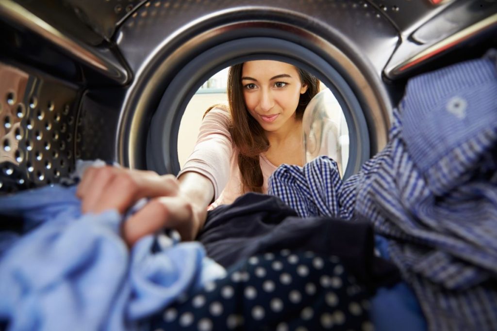 A woman peers through the transparent window of a washing machine, showcasing a moment of intrigue and reflection.